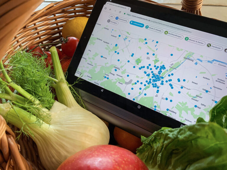 Geöffnete Webseite „München bringt’s“ auf Tablet, welches in Obstkorb liegt.