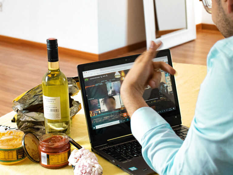 Person sitzt gemütlich mit Snacks und Getränken am Computer und führt ein aktives Gespräch per Videochat.