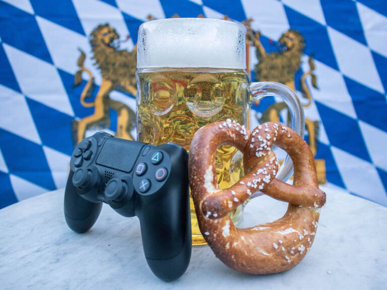 Ein Game-Controller und eine Breze sind an einen Maßkrug angelehnt. Im Hintergrund befindet sich die Bayerische Fahne.