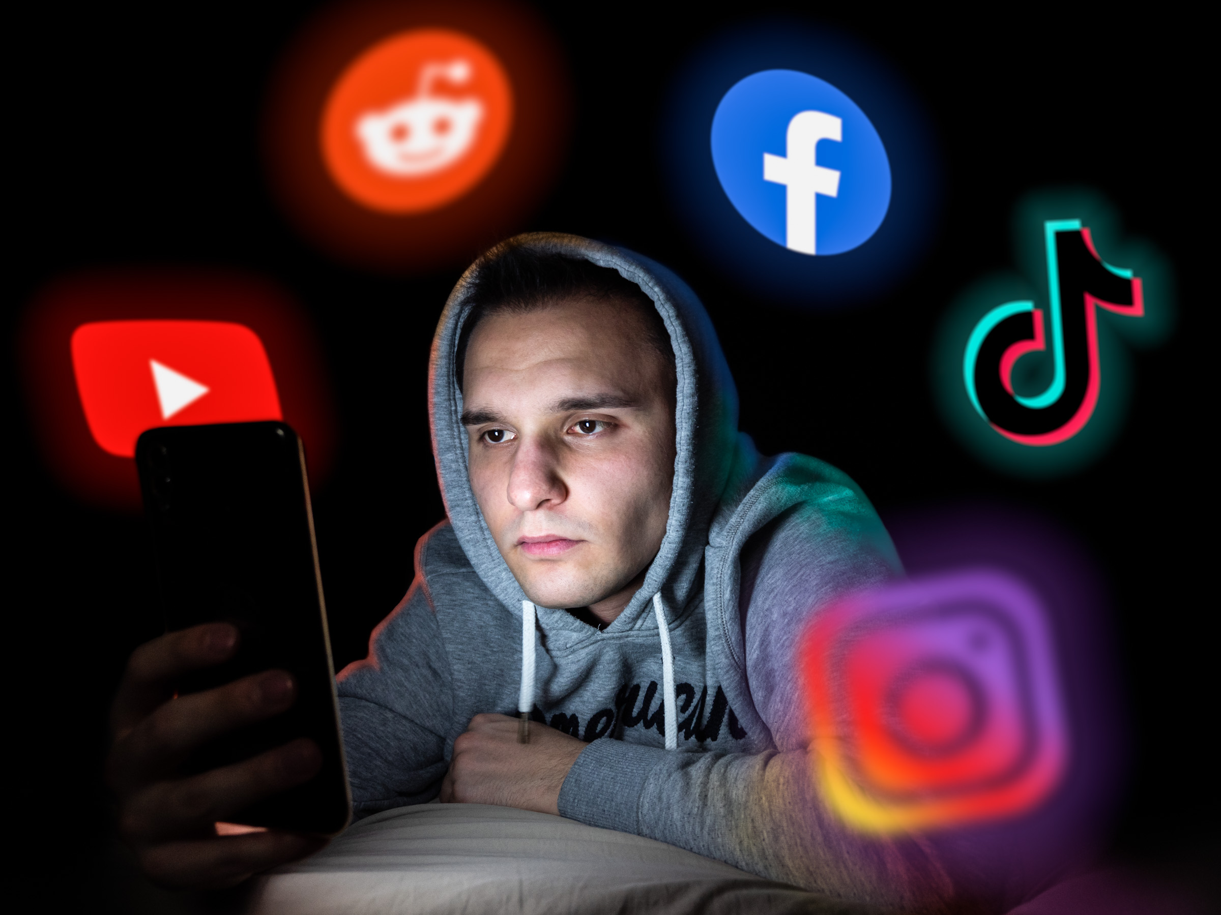 Unmotiviertes Gesicht von Smartphonebildschirm beleuchtet umgeben von Social-Media Logos