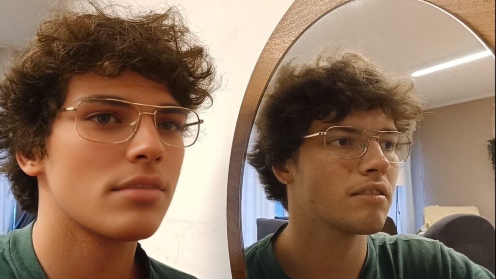 Urheber: Alexander Schmid Foto einer Person neben einem Spiegel. Im Spiegelbild sieht die Person normal aus. In Realität wurde ihr ein starker Schönheitsfilter über das Gesicht gelegt. So soll gezeigt werden, wie Filter das Selbstbild beeinflussen können.